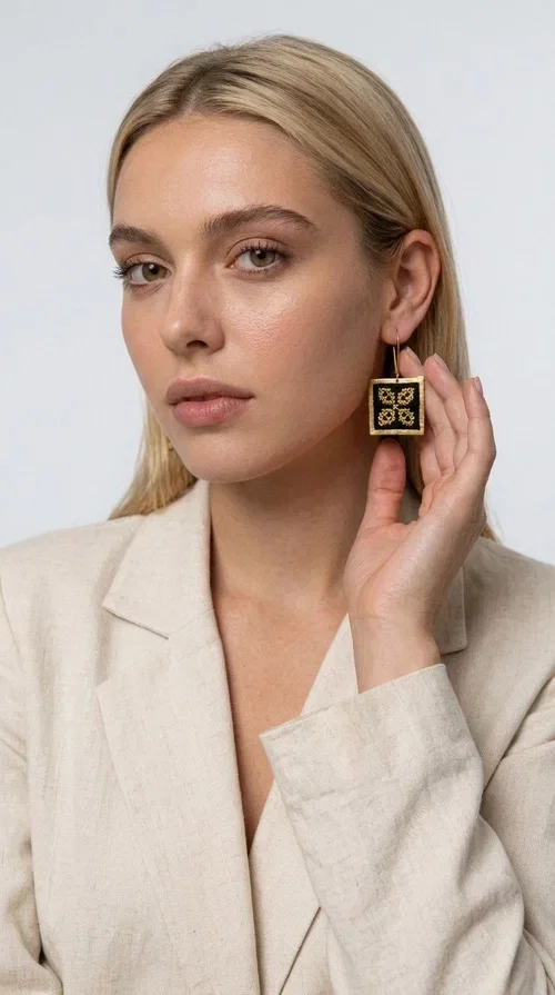 , The embroidered statement earrings with geometric patterns in black are the ideal choice for those seeking a piece of jewelry that combines folk tradition with modern design. Designed by Greek Jewelry Designer Aikaterini Chalkiadaki, these handmade earrings are a unique piece that stands out instantly thanks to their square shape and striking embroidery with golden details on black fabric.

Made from brass and fabric, these earrings feature a geometric motif inspired by folklore aesthetics — four symmetrical embroidered elements in a gold tone are framed by a golden brass frame, creating a result reminiscent of traditional Greek handicrafts. They hang from a gold hook and add movement and character to any look.

Ideal for weddings, christenings, evening outings, or even to elevate a casual everyday look, these statement earrings pair beautifully with both white outfits and neutral colors, as shown in the photo.