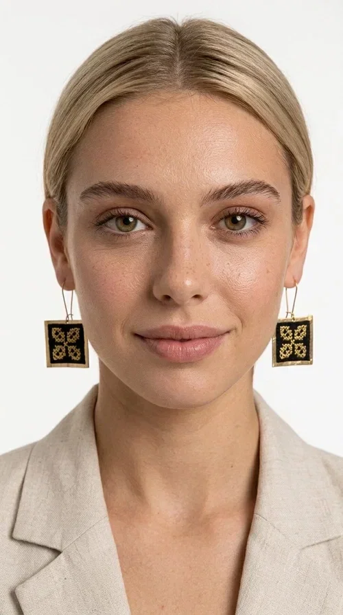 , The embroidered statement earrings with geometric patterns in black are the ideal choice for those seeking a piece of jewelry that combines folk tradition with modern design. Designed by Greek Jewelry Designer Aikaterini Chalkiadaki, these handmade earrings are a unique piece that stands out instantly thanks to their square shape and striking embroidery with golden details on black fabric.

Made from brass and fabric, these earrings feature a geometric motif inspired by folklore aesthetics — four symmetrical embroidered elements in a gold tone are framed by a golden brass frame, creating a result reminiscent of traditional Greek handicrafts. They hang from a gold hook and add movement and character to any look.

Ideal for weddings, christenings, evening outings, or even to elevate a casual everyday look, these statement earrings pair beautifully with both white outfits and neutral colors, as shown in the photo.