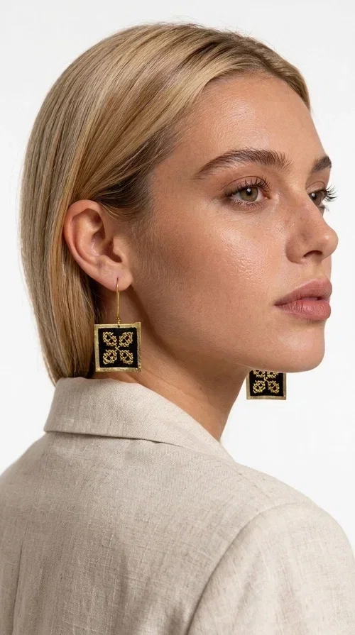 , The embroidered statement earrings with geometric patterns in black are the ideal choice for those seeking a piece of jewelry that combines folk tradition with modern design. Designed by Greek Jewelry Designer Aikaterini Chalkiadaki, these handmade earrings are a unique piece that stands out instantly thanks to their square shape and striking embroidery with golden details on black fabric.

Made from brass and fabric, these earrings feature a geometric motif inspired by folklore aesthetics — four symmetrical embroidered elements in a gold tone are framed by a golden brass frame, creating a result reminiscent of traditional Greek handicrafts. They hang from a gold hook and add movement and character to any look.

Ideal for weddings, christenings, evening outings, or even to elevate a casual everyday look, these statement earrings pair beautifully with both white outfits and neutral colors, as shown in the photo.