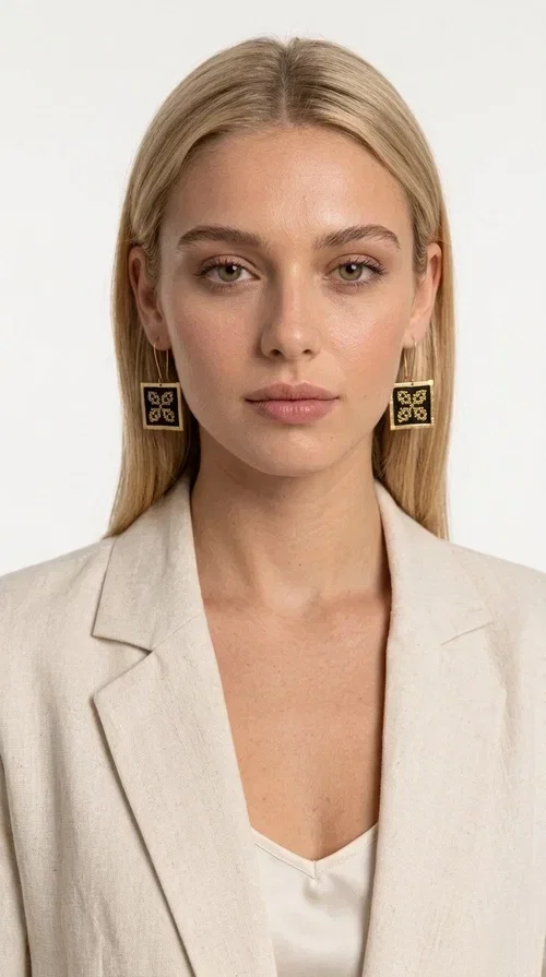 , The embroidered statement earrings with geometric patterns in black are the ideal choice for those seeking a piece of jewelry that combines folk tradition with modern design. Designed by Greek Jewelry Designer Aikaterini Chalkiadaki, these handmade earrings are a unique piece that stands out instantly thanks to their square shape and striking embroidery with golden details on black fabric.

Made from brass and fabric, these earrings feature a geometric motif inspired by folklore aesthetics — four symmetrical embroidered elements in a gold tone are framed by a golden brass frame, creating a result reminiscent of traditional Greek handicrafts. They hang from a gold hook and add movement and character to any look.

Ideal for weddings, christenings, evening outings, or even to elevate a casual everyday look, these statement earrings pair beautifully with both white outfits and neutral colors, as shown in the photo.