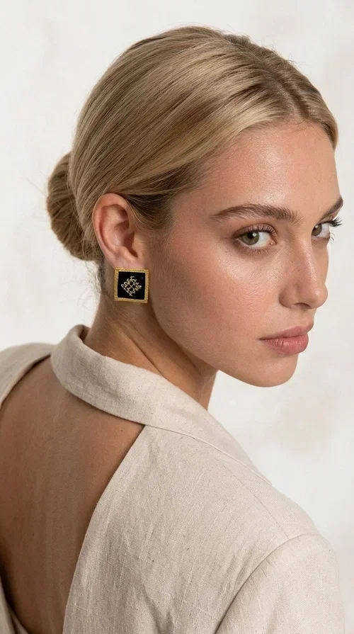 , Embroidered statement earrings with geometric patterns are the ideal choice for anyone who wants to add a touch of individuality and character to their look. The square black fabric with gold embroidered details in a diamond-shaped geometric motif creates a striking result that combines the traditional art of embroidery with modern design. Designed by Greek Jewelry Designer Aikaterini Chalkiadaki, these handmade earrings are a piece with a strong aesthetic identity that evokes folk tradition.

Made of brass and fabric, these earrings combine two materials with different textures and character. The gold brass frame surrounds the black fabric square, while the embroidered geometric pattern gives depth and richness to the composition. The result is a stud earring that is comfortable to wear and automatically becomes the focal point of any look.

They suit both casual and formal looks equally well — from a simple linen jacket to an evening outfit. Also ideal as a gift for women who love unique, handmade jewelry with a Greek aesthetic.