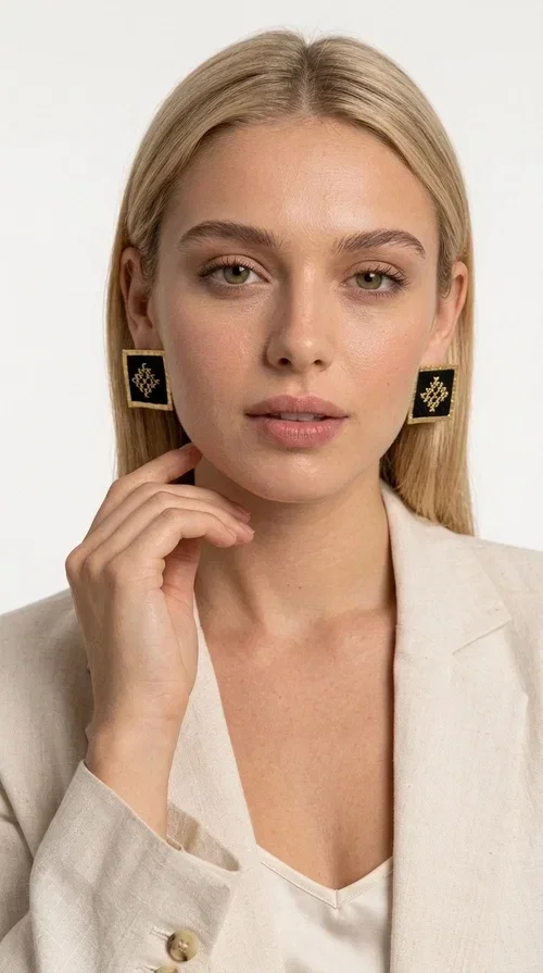, Embroidered statement earrings with geometric patterns are the ideal choice for anyone who wants to add a touch of individuality and character to their look. The square black fabric with gold embroidered details in a diamond-shaped geometric motif creates a striking result that combines the traditional art of embroidery with modern design. Designed by Greek Jewelry Designer Aikaterini Chalkiadaki, these handmade earrings are a piece with a strong aesthetic identity that evokes folk tradition.

Made of brass and fabric, these earrings combine two materials with different textures and character. The gold brass frame surrounds the black fabric square, while the embroidered geometric pattern gives depth and richness to the composition. The result is a stud earring that is comfortable to wear and automatically becomes the focal point of any look.

They suit both casual and formal looks equally well — from a simple linen jacket to an evening outfit. Also ideal as a gift for women who love unique, handmade jewelry with a Greek aesthetic.