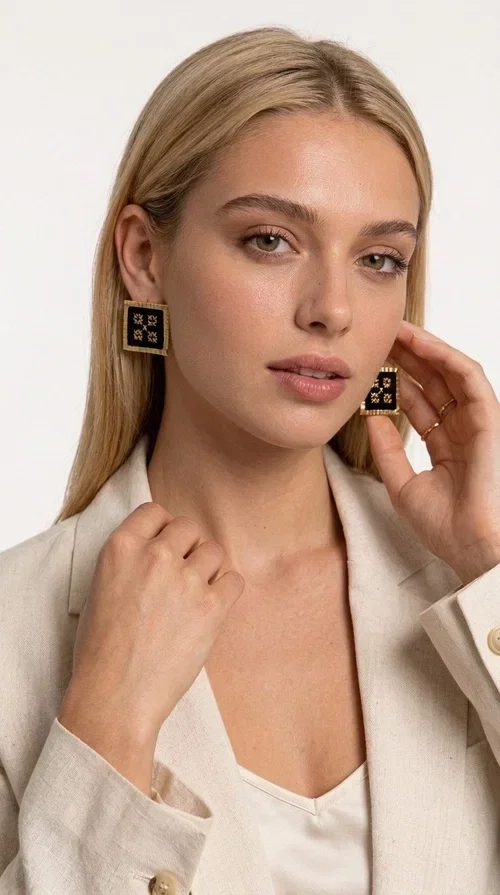 , The embroidered statement earrings with geometric patterns in black are the ideal choice for every woman who wants to express her uniqueness through her accessories. Featuring a square shape, a gold-toned brass frame and embroidered floral motifs on black fabric, these handmade earrings combine the traditional art of embroidery with a modern, striking result. Designed by Greek Jewelry Designer Aikaterini Chalkiadaki, they reflect Greek handcraft tradition with a contemporary touch.

The square brass structure with a gold hue perfectly frames the embroidered piece of fabric, where four symmetrical floral motifs in gold stand out, giving a folklore aesthetic with a bold, statement character. These stud earrings suit both casual and formal looks equally well — from an everyday outfit to a wedding or an evening out.