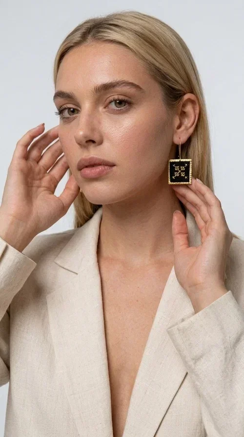 , The embroidered statement earrings with geometric designs in black are the ideal choice for those seeking jewelry with character, texture and history. With a square shape and golden brass frame, they combine the traditional art of embroidery with a modern, minimalist aesthetic result. Designed by Greek Jewelry Designer Aikaterini Chalkiadaki, they draw inspiration from folk tradition and deliver a distinctive folklore style that suits both casual and formal looks.

The black fabric inside the square frame features golden geometric embroidery reminiscent of cross-stitch motifs from traditional handicrafts. The combination of brass and fabric creates an interesting contrast between metal and woven texture, giving the earrings a unique, handmade character. Hanging from a hook, they sit comfortably and strikingly on the ear, making them ideal for everyday wear or special occasions.
