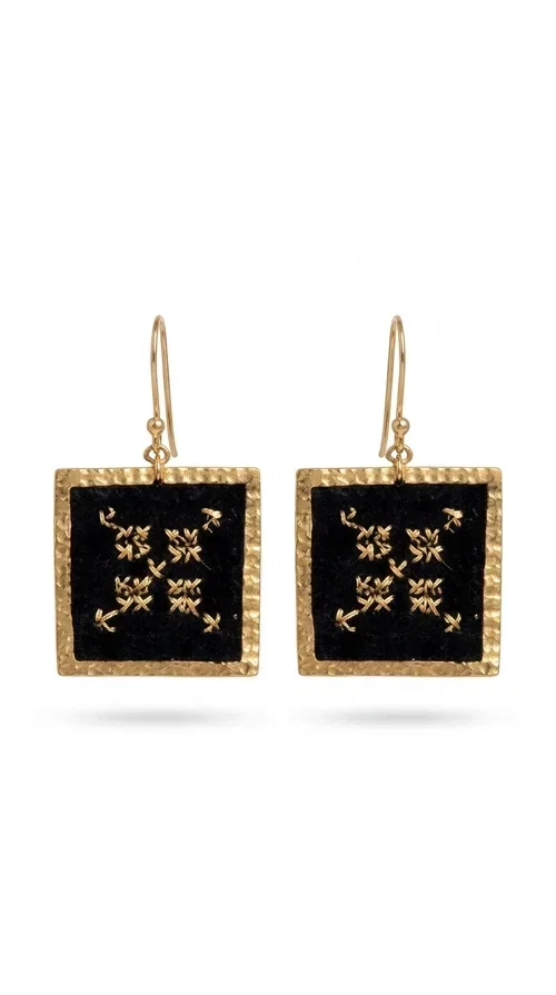 , The embroidered statement earrings with geometric designs in black are the ideal choice for those seeking jewelry with character, texture and history. With a square shape and golden brass frame, they combine the traditional art of embroidery with a modern, minimalist aesthetic result. Designed by Greek Jewelry Designer Aikaterini Chalkiadaki, they draw inspiration from folk tradition and deliver a distinctive folklore style that suits both casual and formal looks.

The black fabric inside the square frame features golden geometric embroidery reminiscent of cross-stitch motifs from traditional handicrafts. The combination of brass and fabric creates an interesting contrast between metal and woven texture, giving the earrings a unique, handmade character. Hanging from a hook, they sit comfortably and strikingly on the ear, making them ideal for everyday wear or special occasions.