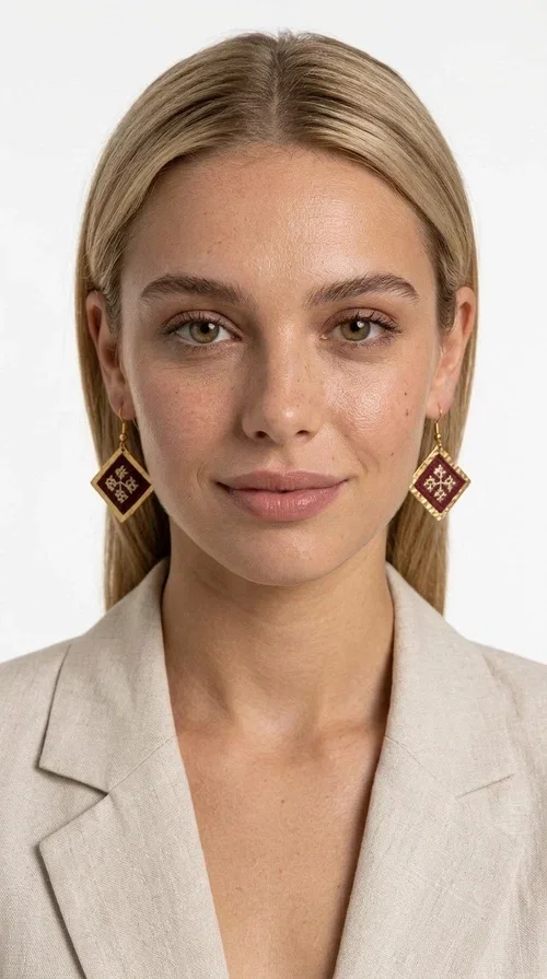 , Embroidered statement earrings with geometric patterns in deep burgundy are the ideal choice for every woman who wants to express herself through her style — with character, color, and a distinctive handmade aesthetic.

Designed by Greek Jewelry Designer Aikaterini Chalkiadaki, these striking dangle earrings combine brass and fabric in a rhombus shape reminiscent of folklore aesthetics and Byzantine tradition. The embroidered floral motif at the center — in golden hues against a deep burgundy background — gives the piece a vintage, boho-chic dimension that suits wedding events, evening outings, and everyday fashion looks alike.

The brass frame with its finely worked gold-toned surface highlights the embroidered fabric, creating a jewel that seems to come from another era — without losing its modern appeal. Lightweight on the ear, hanging from a hook, they pair well with both casual and formal styles, from a linen jacket to an evening dress.