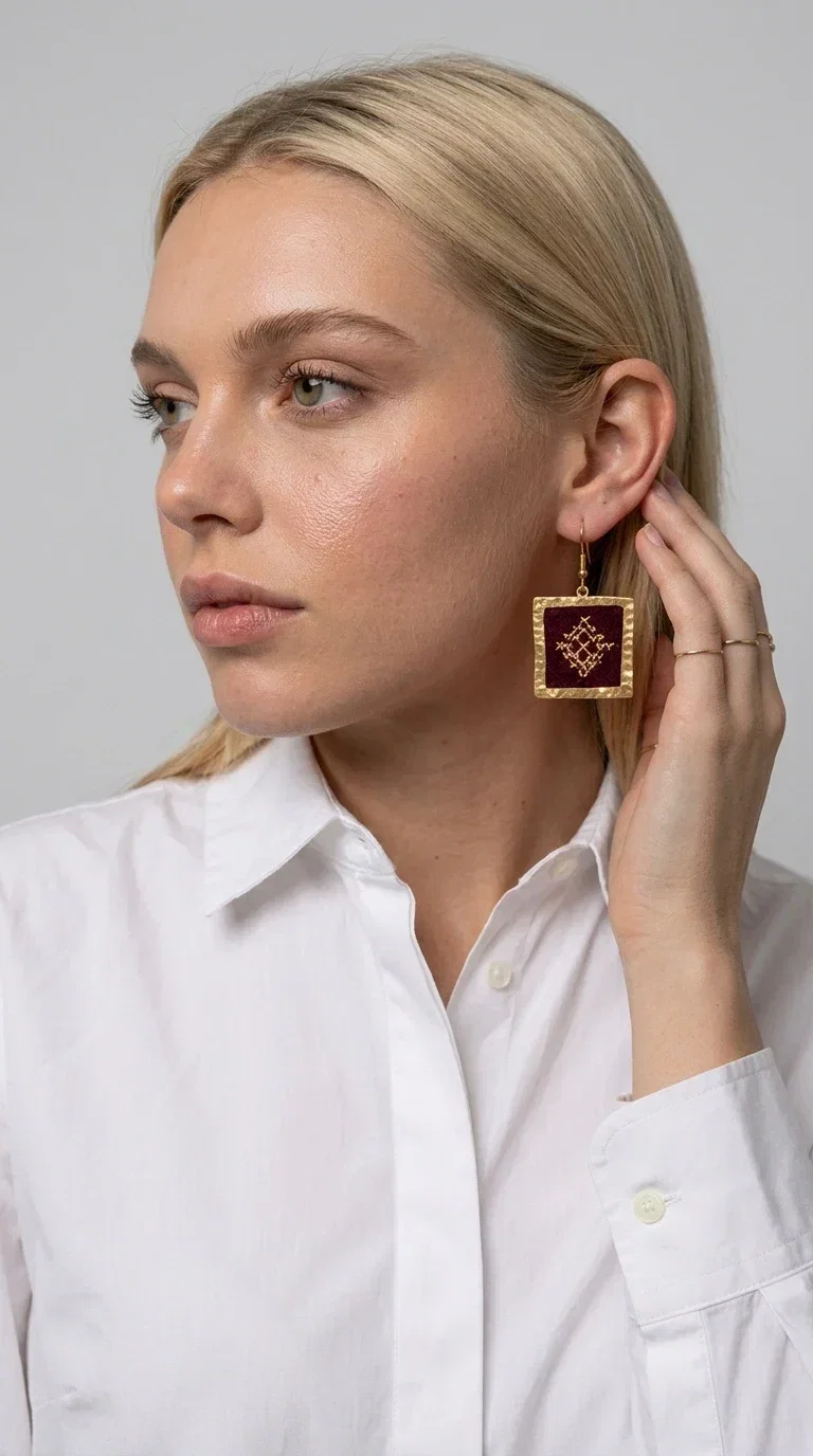 , Embroidered statement earrings in deep burgundy are the ideal choice for every woman looking for jewelry with character and a unique aesthetic. With a square shape and delicate geometric embroidered details in gold, they combine the traditional art of embroidery with a completely modern result — creating a piece of jewelry that stands out.

Designed by Greek Jewelry Designer Aikaterini Chalkiadaki, these handmade earrings are crafted from brass and embroidered fabric, achieving a beautiful combination of materials that evokes a folk aesthetic. The geometric motifs on the embroidered section exude folklore charm, while the golden brass metal frame gives structure and balance to the overall design.

The burgundy embroidered dangle earrings are perfect for evening and formal occasions, such as weddings, christenings and festive events, while also instantly elevating a casual look. The rich burgundy tone makes them especially flattering for all skin tones.