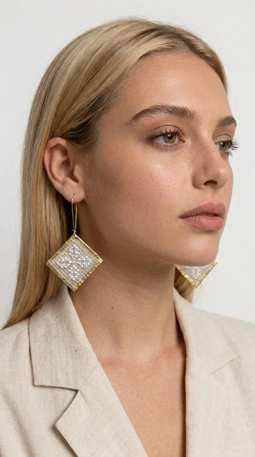 , The embroidered statement earrings with geometric patterns in cream are a bold choice for every woman who loves handmade aesthetics with folk inspiration. Designed by Greek Jewelry Designer Aikaterini Chalkiadaki, these earrings combine the traditional art of embroidery with modern design, creating a truly standout result.

The square-diamond shape with its bold geometric structure and rich embroidered motifs in a cream shade gives off a vintage, elegant feel. The gold-tone brass framing the fabric adds warmth and shine, while the dangling design through a gold-tone hoop ensures comfortable wear. Ideal for weddings, christenings, festive events, and also for casual boho looks that call for a strong statement piece.