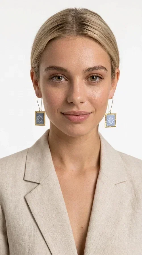 , The embroidered statement earrings with geometric patterns in light blue are the perfect choice for every woman who wants to express her personality in a unique, handmade way. With their striking square shape and finely crafted folk-inspired geometric motifs in shades of light blue, these earrings combine the traditional art of embroidery with a completely modern aesthetic result.

Designed by Greek Jewelry Designer Aikaterini Chalkiadaki, they are handcrafted from brass and fabric, creating a piece of jewelry that highlights the detail and craftsmanship of Greek artistry. The golden brass metal frame surrounds the embroidered fabric featuring light blue geometric motifs with a folklore aesthetic, resulting in a look reminiscent of contemporary boho-chic elegance.

Ideal for weddings, christenings, formal events, but also for everyday chic looks, they pair perfectly with white, ecru, or monochrome outfits. Hanging from a gold-tone hook, they move gently, adding motion and vitality to your look.