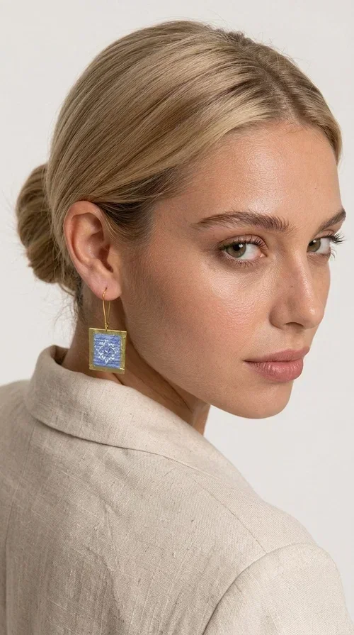 , The embroidered statement earrings with geometric patterns in light blue are the perfect choice for every woman who wants to express her personality in a unique, handmade way. With their striking square shape and finely crafted folk-inspired geometric motifs in shades of light blue, these earrings combine the traditional art of embroidery with a completely modern aesthetic result.

Designed by Greek Jewelry Designer Aikaterini Chalkiadaki, they are handcrafted from brass and fabric, creating a piece of jewelry that highlights the detail and craftsmanship of Greek artistry. The golden brass metal frame surrounds the embroidered fabric featuring light blue geometric motifs with a folklore aesthetic, resulting in a look reminiscent of contemporary boho-chic elegance.

Ideal for weddings, christenings, formal events, but also for everyday chic looks, they pair perfectly with white, ecru, or monochrome outfits. Hanging from a gold-tone hook, they move gently, adding motion and vitality to your look.