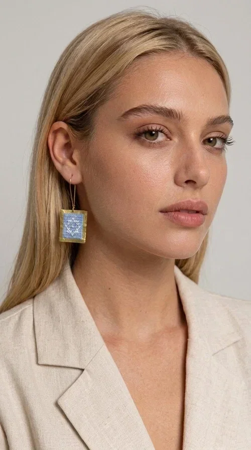 , The embroidered statement earrings with geometric patterns in light blue are the perfect choice for every woman who wants to express her personality in a unique, handmade way. With their striking square shape and finely crafted folk-inspired geometric motifs in shades of light blue, these earrings combine the traditional art of embroidery with a completely modern aesthetic result.

Designed by Greek Jewelry Designer Aikaterini Chalkiadaki, they are handcrafted from brass and fabric, creating a piece of jewelry that highlights the detail and craftsmanship of Greek artistry. The golden brass metal frame surrounds the embroidered fabric featuring light blue geometric motifs with a folklore aesthetic, resulting in a look reminiscent of contemporary boho-chic elegance.

Ideal for weddings, christenings, formal events, but also for everyday chic looks, they pair perfectly with white, ecru, or monochrome outfits. Hanging from a gold-tone hook, they move gently, adding motion and vitality to your look.