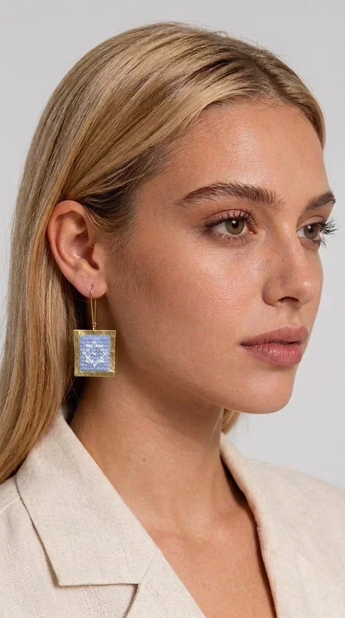 , The embroidered statement earrings with geometric patterns in light blue are the perfect choice for every woman who wants to express her personality in a unique, handmade way. With their striking square shape and finely crafted folk-inspired geometric motifs in shades of light blue, these earrings combine the traditional art of embroidery with a completely modern aesthetic result.

Designed by Greek Jewelry Designer Aikaterini Chalkiadaki, they are handcrafted from brass and fabric, creating a piece of jewelry that highlights the detail and craftsmanship of Greek artistry. The golden brass metal frame surrounds the embroidered fabric featuring light blue geometric motifs with a folklore aesthetic, resulting in a look reminiscent of contemporary boho-chic elegance.

Ideal for weddings, christenings, formal events, but also for everyday chic looks, they pair perfectly with white, ecru, or monochrome outfits. Hanging from a gold-tone hook, they move gently, adding motion and vitality to your look.