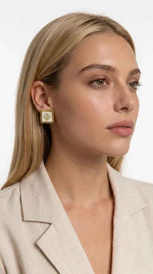 , Embroidered statement earrings with geometric designs in white are the ideal choice for those seeking an accessory that combines traditional craftsmanship with contemporary style. Designed by Greek Jewelry Designer Aikaterini Chalkiadaki, these handmade earrings are a unique piece that exudes authenticity and creativity.

These striking stud earrings feature a square shape with a gold-toned brass frame and white fabric embroidery in geometric patterns inspired by Greek folk tradition. The use of brass and fabric gives them a distinctive boho-folklore character that suits both casual and formal outfits perfectly.

Ideal for weddings, christenings, evening outings, and everyday wear, these embroidered earrings elevate any outfit in a subtly striking way. Pair them with a linen blazer or a boho dress for a complete look.