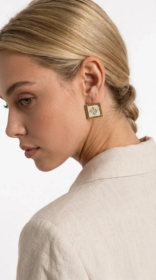, Embroidered statement earrings with geometric designs in white are the ideal choice for those seeking an accessory that combines traditional craftsmanship with contemporary style. Designed by Greek Jewelry Designer Aikaterini Chalkiadaki, these handmade earrings are a unique piece that exudes authenticity and creativity.

These striking stud earrings feature a square shape with a gold-toned brass frame and white fabric embroidery in geometric patterns inspired by Greek folk tradition. The use of brass and fabric gives them a distinctive boho-folklore character that suits both casual and formal outfits perfectly.

Ideal for weddings, christenings, evening outings, and everyday wear, these embroidered earrings elevate any outfit in a subtly striking way. Pair them with a linen blazer or a boho dress for a complete look.
