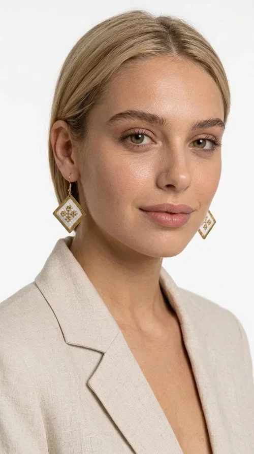 , The embroidered statement earrings with geometric patterns in white and gold are the ideal choice for those seeking a piece of jewelry that combines traditional artistry with contemporary style. Designed by Greek Jewelry Designer Aikaterini Chalkiadaki, these handmade earrings represent a distinctive expression of Greek creativity and craftsmanship.

Their diamond shape, adorned with delicate embroidered decoration on white fabric and gold detailing, evokes the rich tradition of Greek folk art. The combination of brass and fabric creates a piece of jewelry that is light to wear yet striking in presence — perfect for elevating any look, from casual outfits to formal occasions such as weddings or christenings.

These dangling earrings pair perfectly with linen and minimal clothing, adding a boho-ethnic touch of elegance. They also make an excellent gift choice for women who appreciate unique, handmade jewelry with a Greek identity.