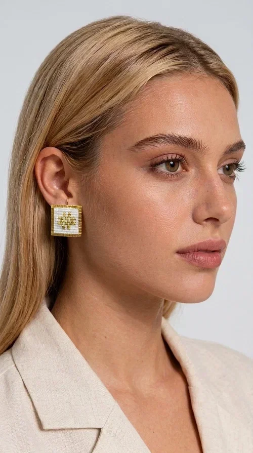 , The embroidered statement earrings with geometric patterns in white are the ideal choice for anyone who wants to express their unique personality through a piece of jewelry with character and soul. Designed by Greek Jewelry Designer Aikaterini Chalkiadaki, these handmade stud earrings combine the traditional art of embroidery with modern aesthetics, creating a result that truly stands out.

Each pair has a square shape and is decorated with a carefully embroidered geometric motif on white fabric, with gold details that highlight the design and add shine. The gold-toned brass frame completes the look harmoniously, while the raised texture of the embroidery adds depth and distinctive character. These are statement pieces that move between folklore and contemporary style.

Ideal for wedding ceremonies, formal occasions, or to elevate a casual outfit, these striking earrings pair equally well with a linen blazer, an evening dress, or a boho ensemble. Thanks to the combination of white and gold, they match almost any color palette.