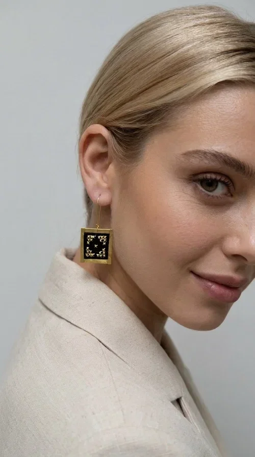 , These embroidered statement earrings with geometric patterns are a bold choice for every woman who wants to express herself through her accessories. Designed by Greek Jewelry Designer Aikaterini Chalkiadaki, these handmade earrings combine the traditional art of embroidery with modern aesthetics, creating a standout result.

The square-shaped gold brass frame encases a black fabric center decorated with handmade embroidery in gold thread, forming an impressive geometric motif inspired by Greek folk tradition. The contrast of the black fabric with the golden details gives the jewelry a vintage yet contemporary feel, equally suited to casual and formal outfits.

Ideal for weddings, christenings, nights out, or to add a unique touch to your everyday look, these earrings hang light and comfortably from the ear thanks to the delicate brass hook.