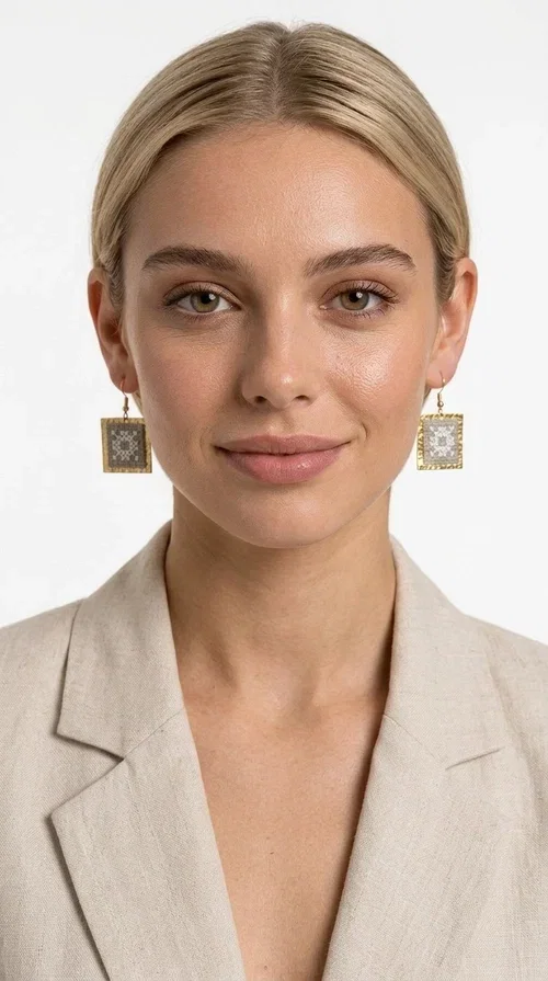, Embroidered statement earrings with geometric patterns in a cream shade are the ideal choice for anyone seeking an accessory that combines the traditional art of embroidery with a modern, eye-catching aesthetic.

Designed by Greek Jewelry Designer Aikaterini Chalkiadaki, these handmade earrings are a unique combination of brass and fabric. Their square shape in a golden hue elegantly frames the embroidered geometric motif at the center, inspired by Greek folk art and tradition. The warm cream tone of the embroidery exudes a timeless elegance that suits both casual and formal looks equally well.

These striking dangle earrings instantly elevate any outfit — from a simple linen jacket to an evening dress for a wedding or christening. They make a perfect gift for women who appreciate craftsmanship and distinctive design.