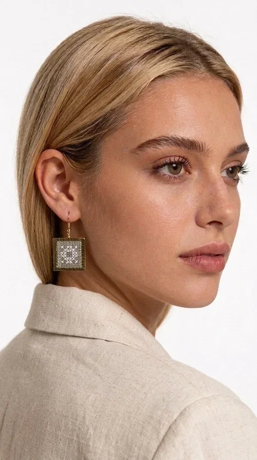 , Embroidered statement earrings with geometric patterns in a cream shade are the ideal choice for anyone seeking an accessory that combines the traditional art of embroidery with a modern, eye-catching aesthetic.

Designed by Greek Jewelry Designer Aikaterini Chalkiadaki, these handmade earrings are a unique combination of brass and fabric. Their square shape in a golden hue elegantly frames the embroidered geometric motif at the center, inspired by Greek folk art and tradition. The warm cream tone of the embroidery exudes a timeless elegance that suits both casual and formal looks equally well.

These striking dangle earrings instantly elevate any outfit — from a simple linen jacket to an evening dress for a wedding or christening. They make a perfect gift for women who appreciate craftsmanship and distinctive design.