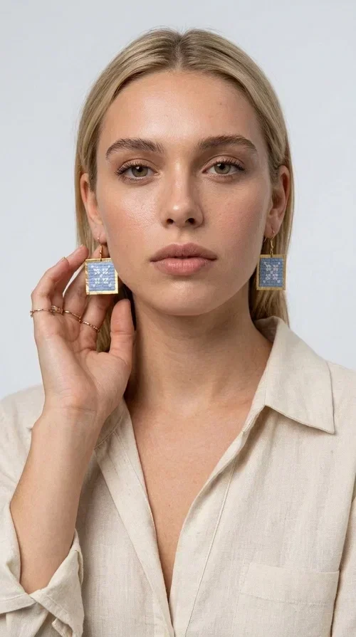 , Embroidered statement earrings in light blue are the ideal choice for anyone who wants to add a touch of color and personality to their everyday or evening look. With a square shape and geometric embroidered motifs inspired by folk tradition, these earrings combine a handmade aesthetic with a modern, boho-folk style. Designed by Greek Jewelry Designer Aikaterini Chalkiadaki, they are a unique piece that carries the soul of Greek craftsmanship.

Made from brass and fabric, the earrings feature a golden metallic frame surrounding a light blue embroidered panel with white geometric details. The combination of materials creates a lightweight piece that is comfortable to wear, even after hours of use. Their square shape and folklore motif make them ideal for women looking for striking earrings with character.

They pair beautifully with casual summer looks, linen outfits, boho dresses, as well as more formal appearances at weddings or christenings. The light blue palette makes them perfect for spring and summer, while their geometric motifs also make them suitable for winter events.