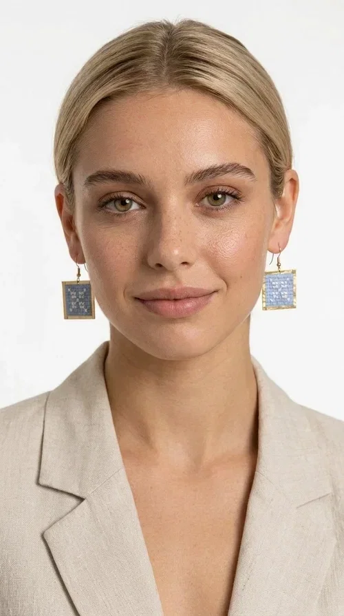 , Embroidered statement earrings in light blue are the ideal choice for anyone who wants to add a touch of color and personality to their everyday or evening look. With a square shape and geometric embroidered motifs inspired by folk tradition, these earrings combine a handmade aesthetic with a modern, boho-folk style. Designed by Greek Jewelry Designer Aikaterini Chalkiadaki, they are a unique piece that carries the soul of Greek craftsmanship.

Made from brass and fabric, the earrings feature a golden metallic frame surrounding a light blue embroidered panel with white geometric details. The combination of materials creates a lightweight piece that is comfortable to wear, even after hours of use. Their square shape and folklore motif make them ideal for women looking for striking earrings with character.

They pair beautifully with casual summer looks, linen outfits, boho dresses, as well as more formal appearances at weddings or christenings. The light blue palette makes them perfect for spring and summer, while their geometric motifs also make them suitable for winter events.