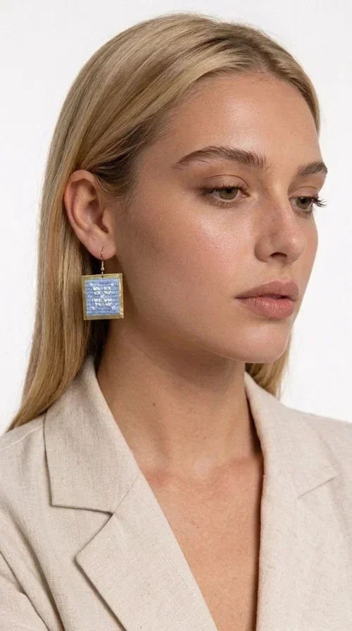 , Embroidered statement earrings in light blue are the ideal choice for anyone who wants to add a touch of color and personality to their everyday or evening look. With a square shape and geometric embroidered motifs inspired by folk tradition, these earrings combine a handmade aesthetic with a modern, boho-folk style. Designed by Greek Jewelry Designer Aikaterini Chalkiadaki, they are a unique piece that carries the soul of Greek craftsmanship.

Made from brass and fabric, the earrings feature a golden metallic frame surrounding a light blue embroidered panel with white geometric details. The combination of materials creates a lightweight piece that is comfortable to wear, even after hours of use. Their square shape and folklore motif make them ideal for women looking for striking earrings with character.

They pair beautifully with casual summer looks, linen outfits, boho dresses, as well as more formal appearances at weddings or christenings. The light blue palette makes them perfect for spring and summer, while their geometric motifs also make them suitable for winter events.