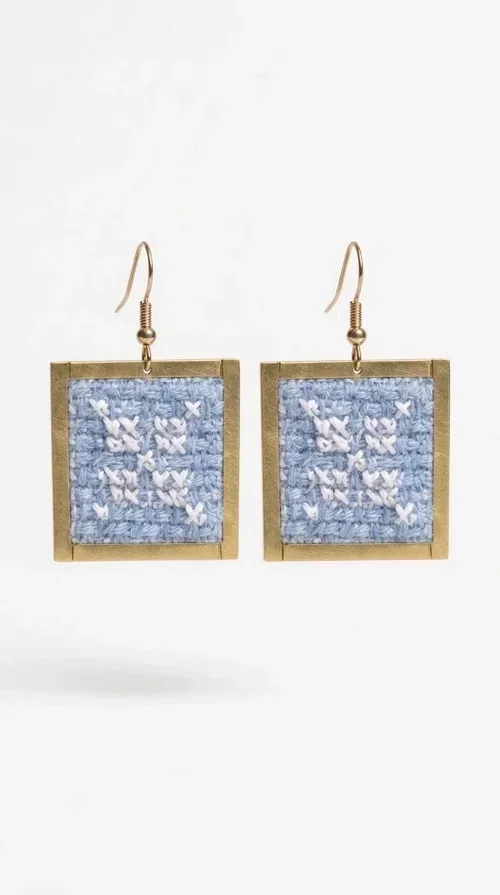 , Embroidered statement earrings in light blue are the ideal choice for anyone who wants to add a touch of color and personality to their everyday or evening look. With a square shape and geometric embroidered motifs inspired by folk tradition, these earrings combine a handmade aesthetic with a modern, boho-folk style. Designed by Greek Jewelry Designer Aikaterini Chalkiadaki, they are a unique piece that carries the soul of Greek craftsmanship.

Made from brass and fabric, the earrings feature a golden metallic frame surrounding a light blue embroidered panel with white geometric details. The combination of materials creates a lightweight piece that is comfortable to wear, even after hours of use. Their square shape and folklore motif make them ideal for women looking for striking earrings with character.

They pair beautifully with casual summer looks, linen outfits, boho dresses, as well as more formal appearances at weddings or christenings. The light blue palette makes them perfect for spring and summer, while their geometric motifs also make them suitable for winter events.