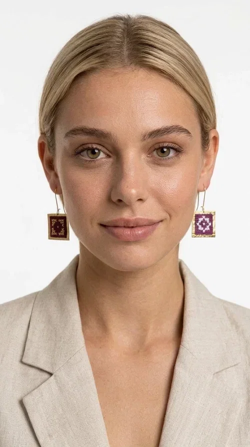 , These embroidered statement earrings with geometric designs in magenta are the ideal choice for those seeking a piece of jewelry that combines folk tradition with contemporary style. Designed by Greek Jewelry Designer Aikaterini Chalkiadaki, these handmade earrings are a distinctive piece that never goes unnoticed.

Each pair features a square shape with a golden brass frame surrounding a fabric panel with traditional cross-stitch embroidery in deep magenta and white. The geometric motif strongly evokes traditional Greek embroidery — a folklore aesthetic that suits both casual and formal looks equally well. They hang from a delicate gold-tone hook, making them comfortable to wear and lightweight on the ear.

Ideal for weddings, christenings, summer outings, and for adding a pop of color to an everyday look. They pair beautifully with neutral outfits — just as shown in the photo, where the vibrant magenta contrasts with a beige jacket for a striking result.