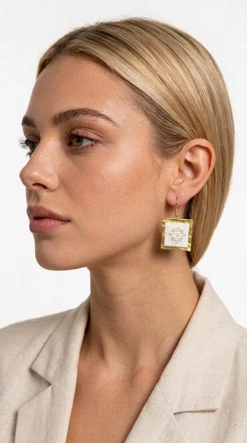 , Embroidered statement earrings with geometric patterns in white are a bold choice for every woman who loves handmade jewelry with character and style. Designed by Greek Jewelry Designer Aikaterini Chalkiadaki, these striking earrings combine the traditional art of embroidery with a modern, geometric aesthetic that stands out.

Made from brass and fabric, the earrings feature a square shape with a gold-toned brass metal frame surrounding a finely embroidered white center adorned with floral and geometric motifs. The result is an accessory that evokes Greek folk tradition while fitting seamlessly into a modern, everyday or festive style.

Ideal for weddings, christenings, nights out, or even to elevate a simple office look, these earrings pair beautifully with linen, boho, or minimal outfits. The white palette makes them versatile and timeless.