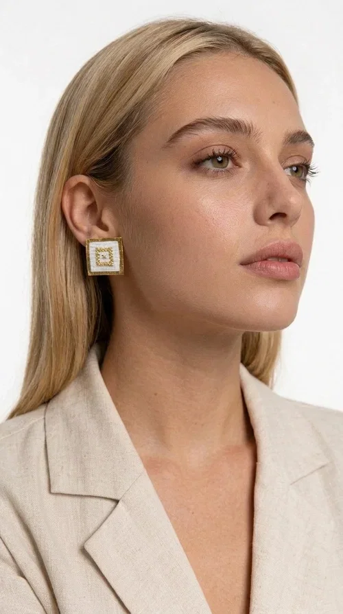 , Embroidered statement earrings with geometric patterns are the ideal choice for those seeking an accessory that combines folk tradition with a modern, minimalist aesthetic. Designed by Greek Jewelry Designer Aikaterini Chalkiadaki, these handmade stud earrings are a tribute to craftsmanship and Greek creativity.

Made from brass and fabric, the earrings feature a square shape on a white background with gold embroidery forming geometric motifs inspired by folk tradition. The result is a jewelry piece with strong character, lightweight to wear and particularly striking in appearance — ideal for both casual outfits and more formal occasions such as weddings, christenings, or professional events.

They pair perfectly with white, beige, or earth-tone clothing, while their square shape adds a modern, geometric element that elevates any look. A perfect gift for women who appreciate handmade jewelry with a Greek soul.