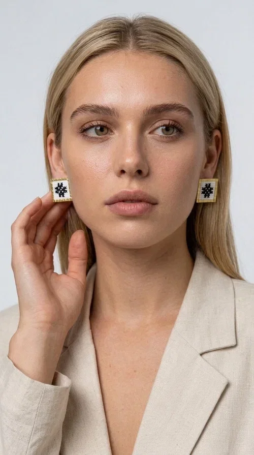 , Embroidered statement earrings with geometric patterns are the ideal choice for those seeking an accessory that combines folk tradition with contemporary style. Designed by Greek Jewelry Designer Aikaterini Chalkiadaki, they are handmade jewelry pieces that highlight the charm of folklore aesthetics in a striking and timeless way.

Each pair features a square shape with a gold brass frame and finely worked embroidery in white and black, forming a geometric snowflake-inspired motif drawn from traditional Greek art. The result is a stud earring that immediately catches the eye, without being overly heavy or bulky — ideal for both everyday and formal wear.

They pair perfectly with casual looks and linen outfits, as well as with formal appearances at weddings, christenings, or summer events. The simplicity of their design makes them versatile, while the embroidery gives them a unique, artisan character.