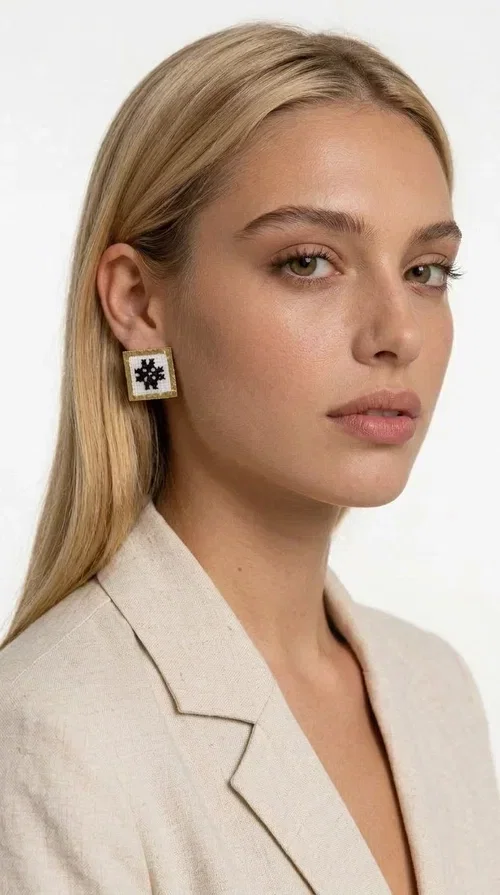 , Embroidered statement earrings with geometric patterns are the ideal choice for those seeking an accessory that combines folk tradition with contemporary style. Designed by Greek Jewelry Designer Aikaterini Chalkiadaki, they are handmade jewelry pieces that highlight the charm of folklore aesthetics in a striking and timeless way.

Each pair features a square shape with a gold brass frame and finely worked embroidery in white and black, forming a geometric snowflake-inspired motif drawn from traditional Greek art. The result is a stud earring that immediately catches the eye, without being overly heavy or bulky — ideal for both everyday and formal wear.

They pair perfectly with casual looks and linen outfits, as well as with formal appearances at weddings, christenings, or summer events. The simplicity of their design makes them versatile, while the embroidery gives them a unique, artisan character.