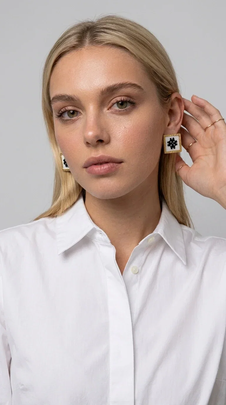 , Embroidered statement earrings with geometric patterns are the ideal choice for those seeking an accessory that combines folk tradition with contemporary style. Designed by Greek Jewelry Designer Aikaterini Chalkiadaki, they are handmade jewelry pieces that highlight the charm of folklore aesthetics in a striking and timeless way.

Each pair features a square shape with a gold brass frame and finely worked embroidery in white and black, forming a geometric snowflake-inspired motif drawn from traditional Greek art. The result is a stud earring that immediately catches the eye, without being overly heavy or bulky — ideal for both everyday and formal wear.

They pair perfectly with casual looks and linen outfits, as well as with formal appearances at weddings, christenings, or summer events. The simplicity of their design makes them versatile, while the embroidery gives them a unique, artisan character.