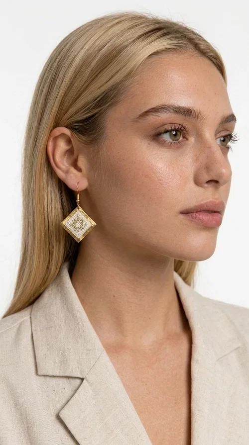 , Embroidered statement earrings with geometric patterns are the ideal choice for every woman who wants to add a folk-chic touch to her look. Designed by Greek Jewelry Designer Aikaterini Chalkiadaki, these handmade earrings combine the tradition of embroidery art with a modern, geometric aesthetic that stands out.

Their diamond shape in white fabric with gold embroidery details and a gold brass frame creates a result that is both elegant and striking. They hang lightly from a gold hook, gently touching the neck and adding movement with every step. Ideal for both everyday wear and special occasions, they pair beautifully with linen and boho outfits, summer dresses, as well as casual-chic looks all year round.