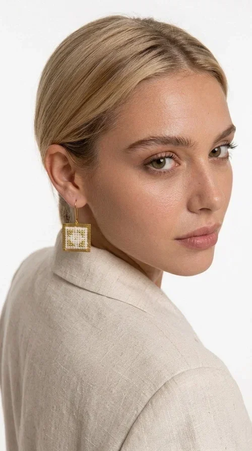 , Embroidered statement earrings with geometric designs are the ideal choice for those seeking an accessory that combines the traditional art of embroidery with contemporary design. Designed by Greek Jewelry Designer Aikaterini Chalkiadaki, these handmade earrings bring Greek aesthetics to the forefront in a bold and modern way.

Each pair features a square embroidered pendant in white with gold geometric details reminiscent of folk-inspired aesthetics. The gold-tone brass frame gives structure and elegance to the piece, while the hook clasp ensures comfortable and secure wear. The result is a piece of jewelry that immediately draws attention without being heavy or bulky.

Ideal for weddings, christenings, festive events, or even to elevate an everyday casual outfit, these particular drop earrings pair equally well with dresses, blazers, and boho-style looks.