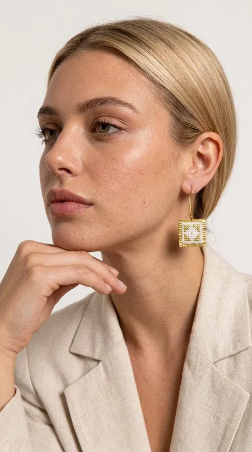 , Embroidered statement earrings with geometric designs are the ideal choice for those seeking an accessory that combines the traditional art of embroidery with contemporary design. Designed by Greek Jewelry Designer Aikaterini Chalkiadaki, these handmade earrings bring Greek aesthetics to the forefront in a bold and modern way.

Each pair features a square embroidered pendant in white with gold geometric details reminiscent of folk-inspired aesthetics. The gold-tone brass frame gives structure and elegance to the piece, while the hook clasp ensures comfortable and secure wear. The result is a piece of jewelry that immediately draws attention without being heavy or bulky.

Ideal for weddings, christenings, festive events, or even to elevate an everyday casual outfit, these particular drop earrings pair equally well with dresses, blazers, and boho-style looks.