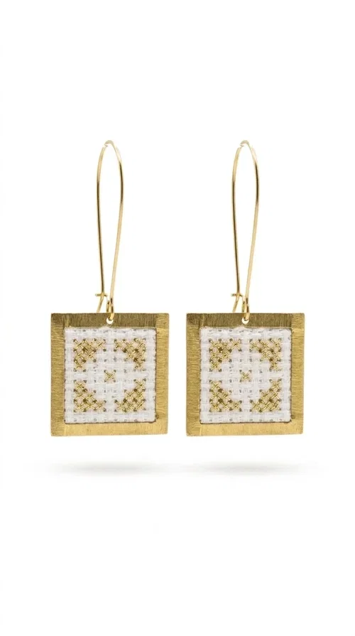 , Embroidered statement earrings with geometric designs are the ideal choice for those seeking an accessory that combines the traditional art of embroidery with contemporary design. Designed by Greek Jewelry Designer Aikaterini Chalkiadaki, these handmade earrings bring Greek aesthetics to the forefront in a bold and modern way.

Each pair features a square embroidered pendant in white with gold geometric details reminiscent of folk-inspired aesthetics. The gold-tone brass frame gives structure and elegance to the piece, while the hook clasp ensures comfortable and secure wear. The result is a piece of jewelry that immediately draws attention without being heavy or bulky.

Ideal for weddings, christenings, festive events, or even to elevate an everyday casual outfit, these particular drop earrings pair equally well with dresses, blazers, and boho-style looks.