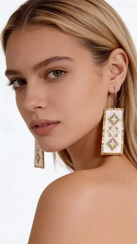 , These striking statement earrings, embroidered with gold thread, combine the traditional art of embroidery with a modern aesthetic. Designed by Greek Jewelry Designer Aikaterini Chalkiadaki, these handmade earrings are adorned with geometric motifs on a white base, creating an elegant and timeless look.

The dangle earrings feature detailed gold embroidered decoration forming diamond-shaped patterns, offering unique texture and volume. The white base creates the perfect contrast with the gold details, while their rectangular shape makes them ideal for any occasion.

These modern embroidered earrings are the perfect choice for women who love striking jewelry with traditional elements. They pair harmoniously with both classic and contemporary outfits, adding a touch of elegance and originality. Store in a dry place and clean gently with a dry cloth.