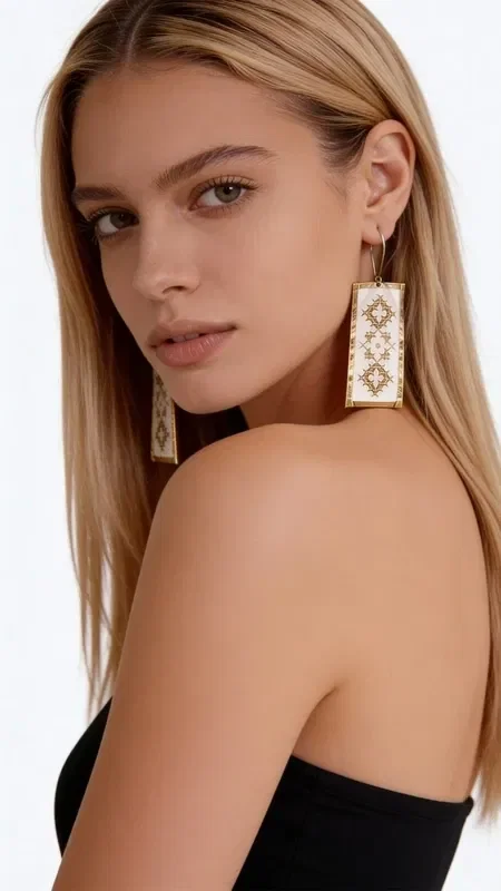 , These striking statement earrings, embroidered with gold thread, combine the traditional art of embroidery with a modern aesthetic. Designed by Greek Jewelry Designer Aikaterini Chalkiadaki, these handmade earrings are adorned with geometric motifs on a white base, creating an elegant and timeless look.

The dangle earrings feature detailed gold embroidered decoration forming diamond-shaped patterns, offering unique texture and volume. The white base creates the perfect contrast with the gold details, while their rectangular shape makes them ideal for any occasion.

These modern embroidered earrings are the perfect choice for women who love striking jewelry with traditional elements. They pair harmoniously with both classic and contemporary outfits, adding a touch of elegance and originality. Store in a dry place and clean gently with a dry cloth.