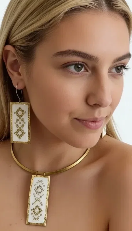 , These striking statement earrings, embroidered with gold thread, combine the traditional art of embroidery with a modern aesthetic. Designed by Greek Jewelry Designer Aikaterini Chalkiadaki, these handmade earrings are adorned with geometric motifs on a white base, creating an elegant and timeless look.

The dangle earrings feature detailed gold embroidered decoration forming diamond-shaped patterns, offering unique texture and volume. The white base creates the perfect contrast with the gold details, while their rectangular shape makes them ideal for any occasion.

These modern embroidered earrings are the perfect choice for women who love striking jewelry with traditional elements. They pair harmoniously with both classic and contemporary outfits, adding a touch of elegance and originality. Store in a dry place and clean gently with a dry cloth.