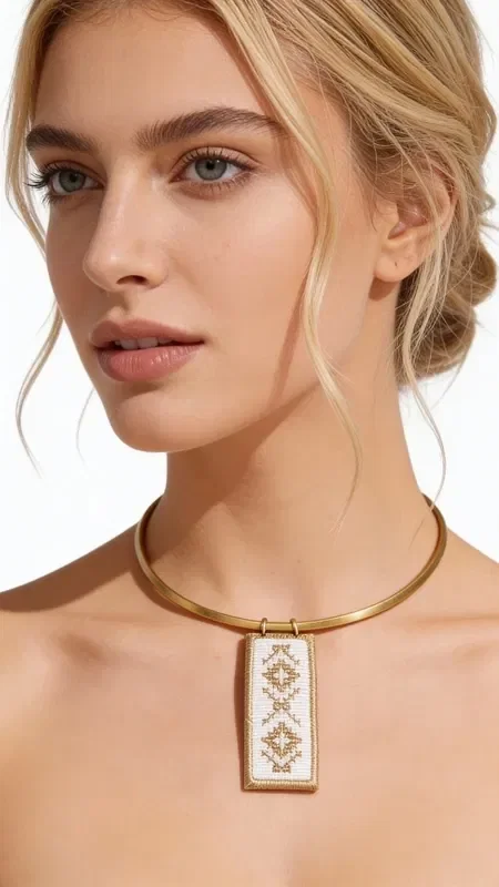 , Discover the art of embroidery in jewelry with this exceptional embroidered white necklace that combines traditional technique with contemporary design. Designed by Greek Jewelry Designer Aikaterini Chalkiadaki, this unique piece features geometric patterns embroidered with gold thread on white fabric, creating a striking contrast that catches the eye.

The statement necklace features a square pendant surface that proudly showcases the handmade geometric motifs, complemented by a gold metal brass collar that adds elegance and stability. The white base with gold thread creates a perfect combination that pairs ideally with summer outfits and bohemian style.

Ideal for both day and evening looks, this embroidered necklace adds an artistic character to your style. It is easy to maintain with gentle cleaning and storage in a dry environment.