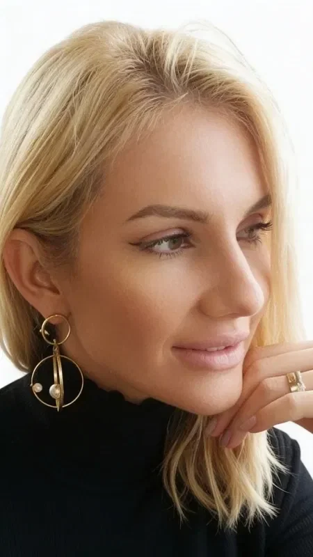 , Discover the magic of three-dimensional statement earrings that highlight your femininity in a striking way. These unique handmade dangle hoop earrings, crafted from brass and designed by Greek Jewelry Designer Aikaterini Chalkiadaki, combine modern aesthetics with the classic elegance of pearls.

The innovative geometric design features a system of gold-tone hoops that create a stunning visual effect, while the natural pearls add a touch of luxury. Each earring has two layers of hoops connected by a vertical bar, creating a three-dimensional structure ideal for those who love eye-catching accessories.

These large earrings are the perfect choice for bridal looks, evening outings, or any moment you want to stand out. The golden hue of the brass suits all skin tones and pairs easily with any style of dressing.