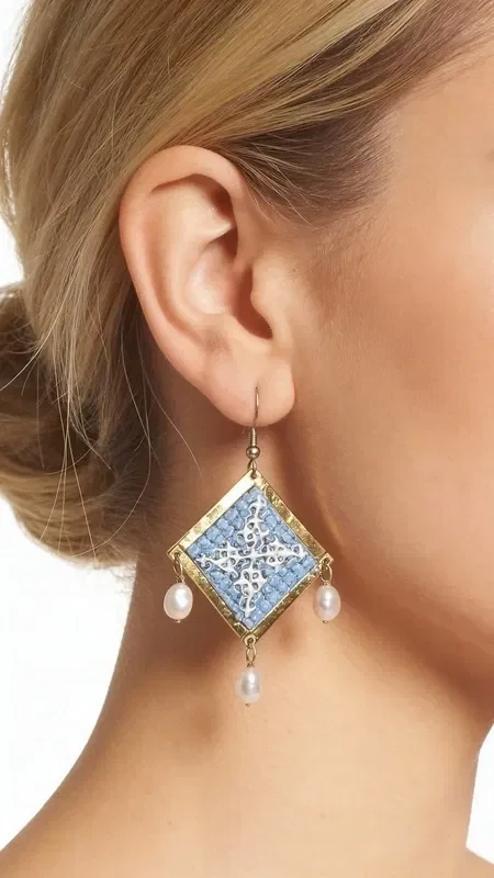, These statement embroidered earrings in light blue with geometric patterns made of gold thread are the ideal handmade jewelry piece to highlight your uniqueness. These impressive dangle earrings, designed by Greek Jewelry Designer Aikaterini Chalkiadaki, combine the traditional art of embroidery with a modern aesthetic.

The light blue hue combined with the gold thread creates a refined contrast that catches the eye. The geometric patterns add a contemporary touch, while the delicate pearls hanging from the base of the earrings add movement and femininity. Their folklore design makes them ideal for special occasions, from bridal looks to cocktail parties. Perfect earrings for weddings, christenings, and special events. Care for them with attention, avoiding contact with water and perfumes for a longer lifespan.