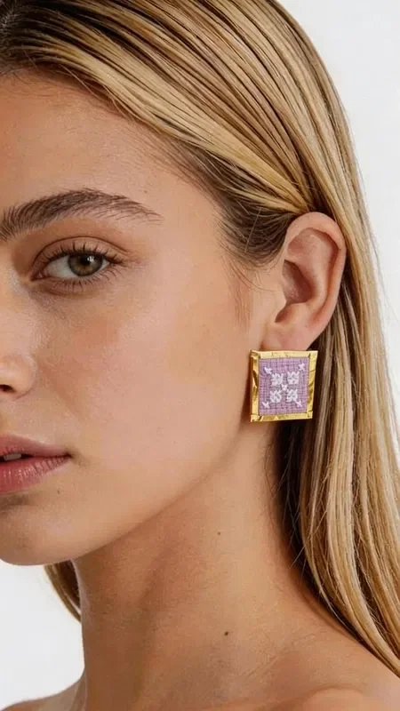 , These embroidered statement earrings with geometric patterns in a lilac shade will become your favorite accessory for every special occasion. Designed by Greek Jewelry Designer Aikaterini Chalkiadaki, these striking handmade earrings combine the traditional art of embroidery with contemporary design. The square shape with intricate geometric motifs creates a unique visual effect, while the gold thread adds shine and elegance. The romantic lilac color highlights femininity and offers versatility when pairing with different outfits. These modern embroidered earrings are ideal for weddings, evening outings, and for elevating your everyday look. The handmade construction guarantees the uniqueness and quality of each piece.

Material: Brass, Fabric

Care: Store the earrings in a dry place and avoid contact with water and cosmetics to preserve the shine of the gold thread.