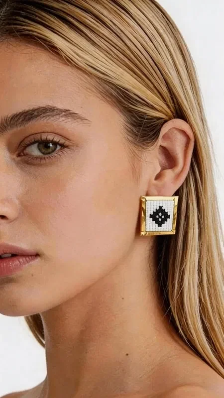 , Stand out with these striking statement earrings, embroidered with geometric patterns in white, combining the traditional art of goldwork embroidery with contemporary design. Designed by Greek Jewelry Designer Aikaterini Chalkiadaki, these handmade earrings are the perfect choice for any woman who wants to express her personality with style.

The embroidered geometric motif in white and black creates a striking visual contrast that catches every eye. The gold-tone base adds luxury and elegance, while their square shape makes them ideal for modern looks. These statement earrings pair perfectly with professional outfits, casual looks, or wedding ceremonies.

Material: Brass, Fabric

Care for your earrings by storing them in a dry place and cleaning them gently with a soft cloth. Avoid contact with perfumes and moisture to preserve their beauty for years to come.