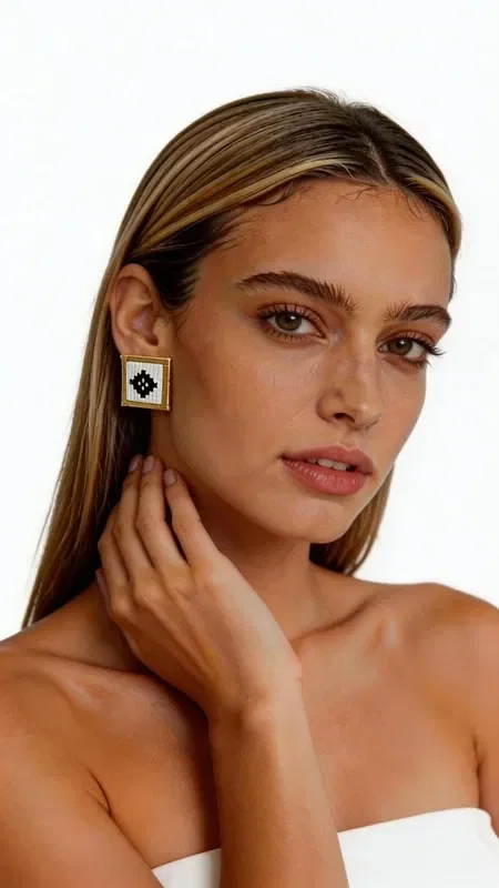 , Stand out with these striking statement earrings, embroidered with geometric patterns in white, combining the traditional art of goldwork embroidery with contemporary design. Designed by Greek Jewelry Designer Aikaterini Chalkiadaki, these handmade earrings are the perfect choice for any woman who wants to express her personality with style.

The embroidered geometric motif in white and black creates a striking visual contrast that catches every eye. The gold-tone base adds luxury and elegance, while their square shape makes them ideal for modern looks. These statement earrings pair perfectly with professional outfits, casual looks, or wedding ceremonies.

Material: Brass, Fabric

Care for your earrings by storing them in a dry place and cleaning them gently with a soft cloth. Avoid contact with perfumes and moisture to preserve their beauty for years to come.