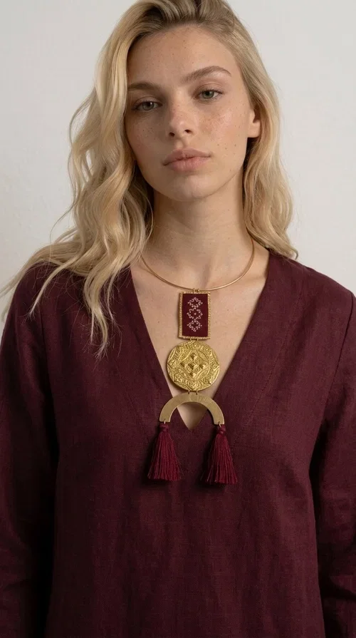 , A statement embroidered necklace that combines tradition with contemporary aesthetics — ideal for every woman who loves striking jewelry with character.

Designed by Greek Jewelry Designer Aikaterini Chalkiadaki, this handmade necklace is a harmonious composition of brass and fabric in a deep burgundy color. The embroidered rectangular piece with folklore-inspired geometric patterns sets the tone, while the round engraved metal piece and the semicircular base with burgundy tassels complete a composition rich in texture and detail. The necklace is worn on a gold-toned torque — clasp-free, lightweight and comfortable to wear.

Ideal for pairing with white linen or a monochrome outfit, it instantly adds character to both casual and evening looks. The geometric embroidery and tassels make it a distinctive piece — a true statement jewelry piece for the neck.