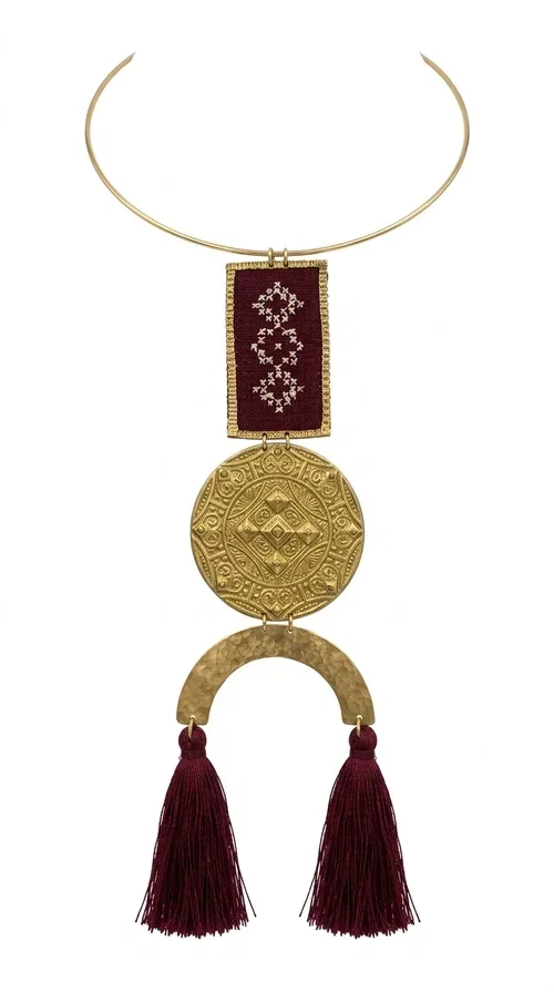 , A statement embroidered necklace that combines tradition with contemporary aesthetics — ideal for every woman who loves striking jewelry with character.

Designed by Greek Jewelry Designer Aikaterini Chalkiadaki, this handmade necklace is a harmonious composition of brass and fabric in a deep burgundy color. The embroidered rectangular piece with folklore-inspired geometric patterns sets the tone, while the round engraved metal piece and the semicircular base with burgundy tassels complete a composition rich in texture and detail. The necklace is worn on a gold-toned torque — clasp-free, lightweight and comfortable to wear.

Ideal for pairing with white linen or a monochrome outfit, it instantly adds character to both casual and evening looks. The geometric embroidery and tassels make it a distinctive piece — a true statement jewelry piece for the neck.