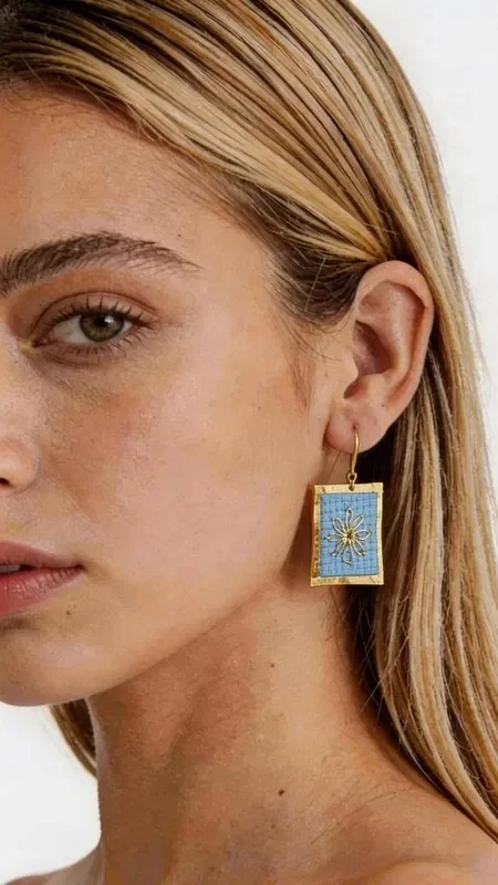 , The statement embroidered earrings with geometric patterns in gold thread on light blue are a unique combination of traditional craftsmanship and modern design. Designed by Greek Jewelry Designer Aikaterini Chalkiadaki, these striking handmade earrings enhance the elegance of any look with style and character. The delicate embroidery technique with gold thread creates a beautiful effect that subtly shimmers, while the light blue color offers a freshness that pairs perfectly with spring and summer outfits. The geometric patterns give a modern aesthetic, making these striking earrings an ideal choice for any occasion. The handmade embroidered earrings are perfect for weddings, christenings, summer parties and every special moment where you want to stand out. Pair them with white or blue clothing to highlight their light blue color. Material: Brass, Fabric. Take care of your earrings by storing them in a dry place, away from moisture and direct sunlight, to preserve their shine.
