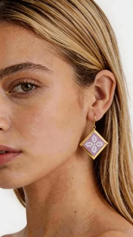 , These statement embroidered earrings in a soft lilac shade with geometric patterns in gold thread are the perfect choice for adding a touch of elegance and originality to your look. Designed by Greek Jewelry Designer Aikaterini Chalkiadaki, these handmade earrings combine the traditional technique of embroidery with contemporary design. Their square geometric shape is adorned with intricately embroidered motifs in a soft lilac tone, while the gold outline adds a luxurious touch. The folklore design with its detailed geometric patterns creates a unique piece of jewelry that stands out and complements both casual and formal looks. Ideal for women who love statement accessories, these earrings are perfect for special occasions, weddings, or for adding a splash of color to your everyday style.

Material: Brass, Fabric. To care for them, store the earrings in a dry place and avoid contact with water and chemicals.